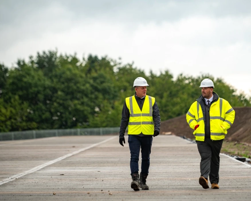 Four people in high-vis jackets and helmets walking in front of an in-progress build project