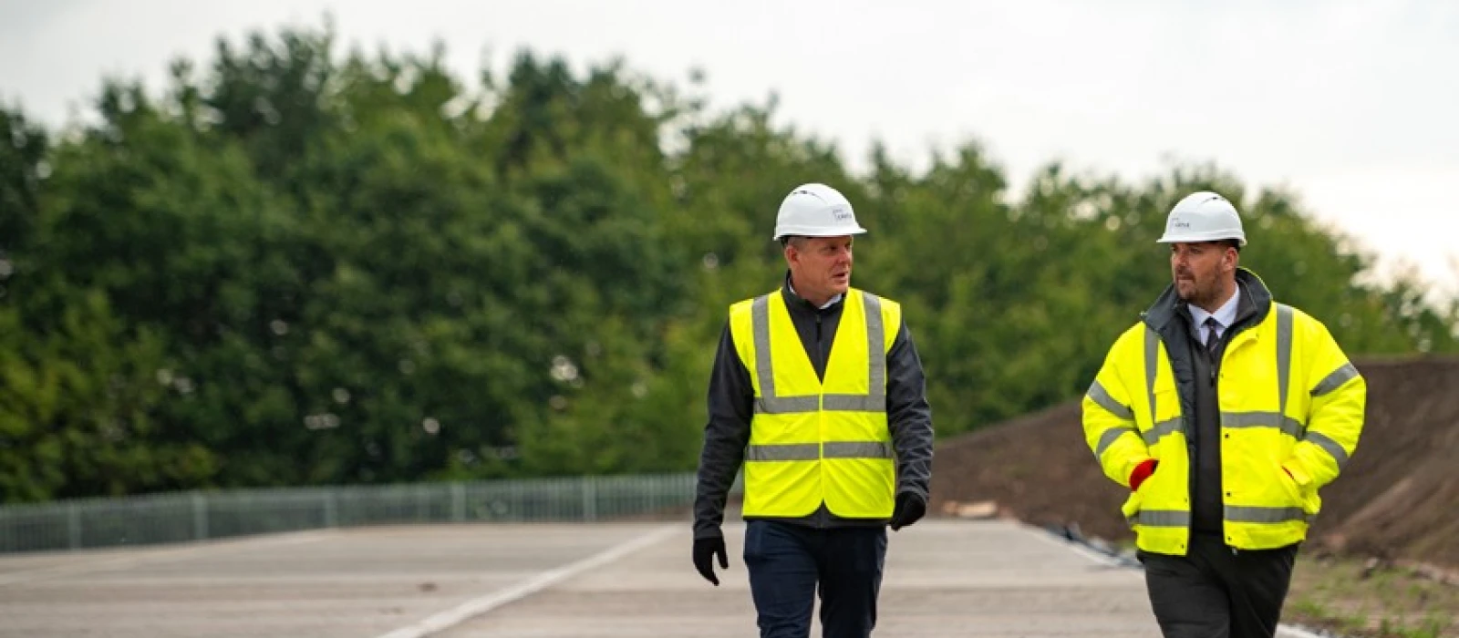 Four people in high-vis jackets and helmets walking in front of an in-progress build project