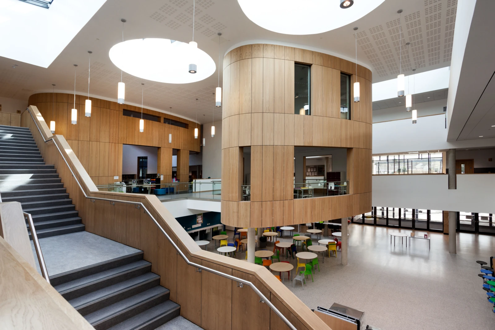 A large interior with a curved wooden paneled upper floor standing on pillars above a cafe area