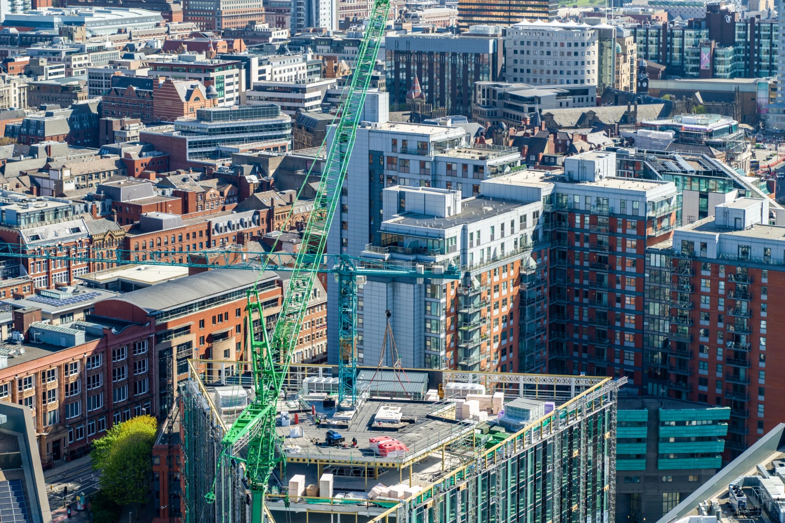 A large green crane on top of a skyscraper being built